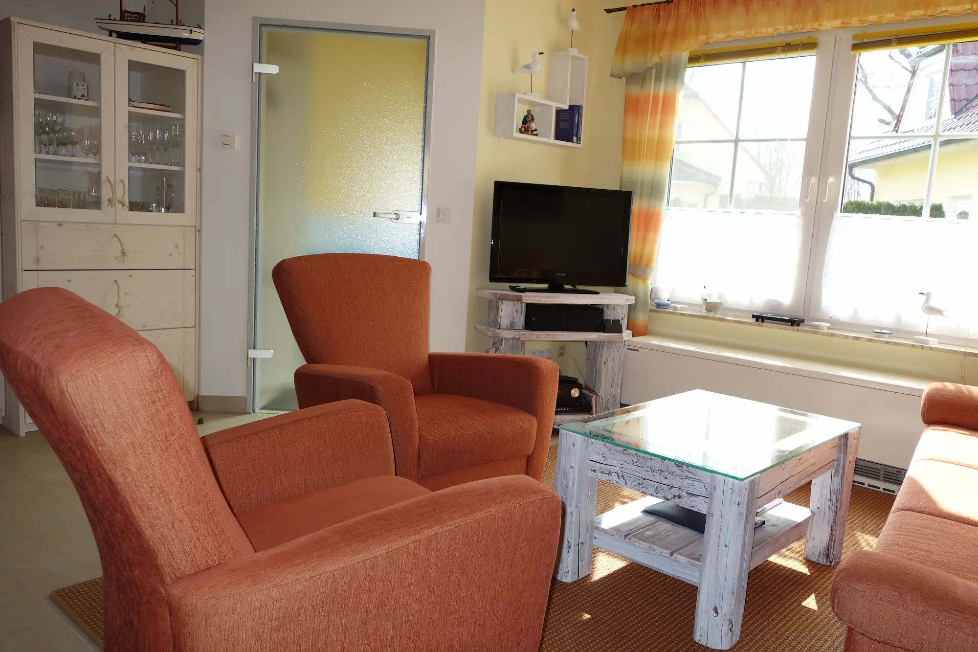 Helles Wohnzimmer im Ferienhaus Am Deich 25 in Zingst mit Sesseln, Couchtisch, TV und großem Fenster.