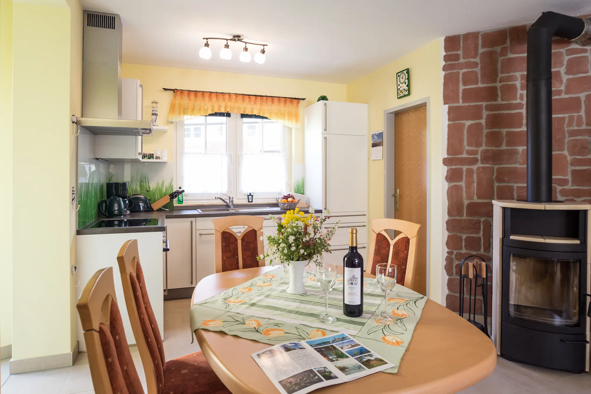 Essbereich mit Esstisch im Ferienhaus Am Deich 25, daneben die Küche und ein Kaminofen im Erdgeschoss.