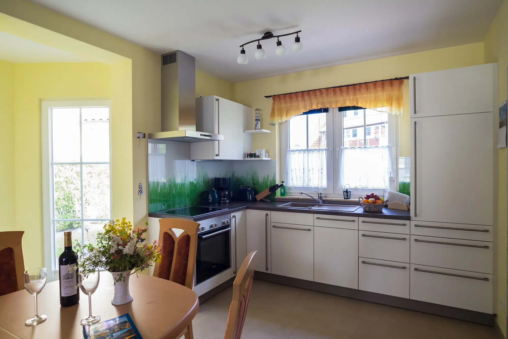 Helle Küche im Ferienhaus Am Deich 25 mit großem Fenster, Arbeitsfläche und Esstisch im Vordergrund.