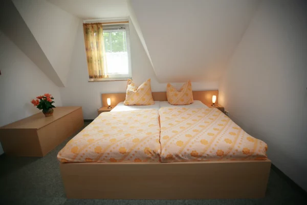 Schlafzimmer im Obergeschoss des Ferienhauses Am Deich 25 in Zingst mit Doppelbett, Nachttischlampen und Fenster.