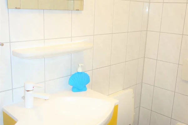 Gäste-WC im Ferienhaus Am Deich 25 mit Waschbecken, Spiegel und WC in hell gefliestem Raum.